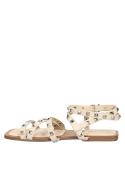 Calzado femenino moderno con correas cruzadas y tachas audaces sobre cuero beige, ideal para un look rockero.