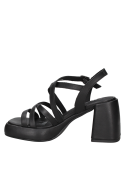 Sandalia de cuero negro con hebilla ajustable lateral, proporcionando estabilidad y confort con su taco ancho y alto.