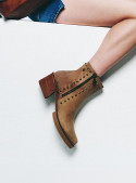 Botín de cuero camel con cierre lateral y tachas, corte medio al tobillo, ideal para un look moderno.