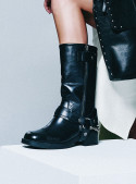 Bota negra biker de cuero para mujer con cremallera lateral y correa metálica en el tobillo, robusta y elegante.
